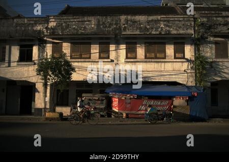 Un rickshaw ciclabile che si muove su una strada vuota, passando di fronte ad un venditore di cibo lungo la strada nella parte vecchia di Sibolga, una città si trova sulla costa occidentale di Sumatra nella provincia di Sumatra del Nord, Indonesia. Foto Stock