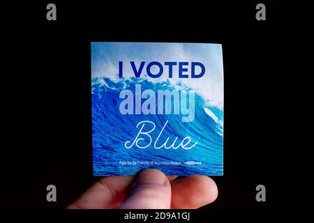 3 novembre 2020 - Elkins Park, Pennsylvania: Un adesivo del giorno delle elezioni tenuto da una mano che dice che ho votato Blu con un'onda in background su Nero Foto Stock