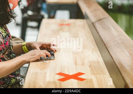 Donna che usa telefoni cellulari per lavorare con immagine sfocata di il contrassegno di posto alternativo per la distanza sociale regola la distanza per uno sedile da altre persone a. Foto Stock