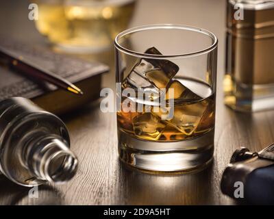 Vetro retroilluminato di whisky sulle rocce su un tavolo di legno, con taccuino, penna e matraccio Foto Stock