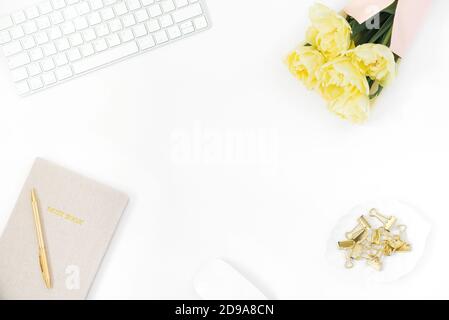 Scrivania da donna stilizzata, scrivania da ufficio. Uno spazio di lavoro con un computer, un bouquet di tulipani gialli, una clipboard, un blocco note per le note e una penna a sfera. WOM Foto Stock