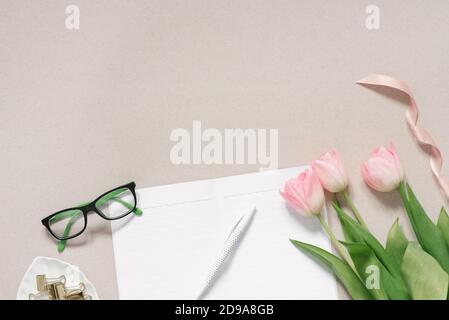 Vista dall'alto sfondo femminile. Tulipani rosa, pagine vuote di un diario aperto, bicchieri e penne su sfondo di caffè. Posti di lavoro piani per le donne d'affari, bl Foto Stock