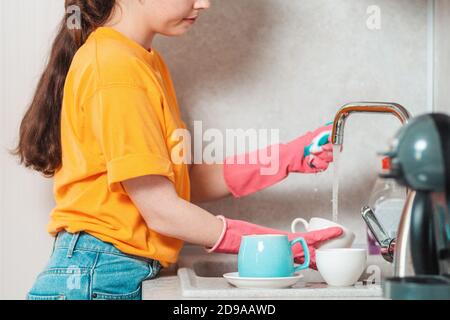 Primo piano ritratto di donna in abiti casual e guanti di gomma rosa è lavaggio piatti. Vista laterale. Lavoro di casa. Foto Stock