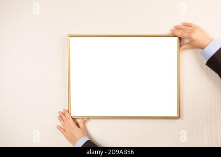 cornice vuota appesa su una parete beige. Mani che appendono il mockup della cornice fotografica sulla parete. Giovane donna con cornice vuota con copyspace Foto Stock