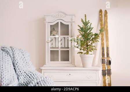 Decorazioni natalizie nel soggiorno: Cassettiera, sci, sedia con una coperta e un abete rosso in vaso Foto Stock