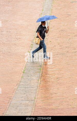 Un uomo che tiene un ombrello cammina attraverso Piazza del campo sotto la pioggia, Siena, Toscana, Italia Foto Stock