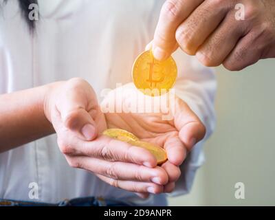 La mano di un uomo ha preso una moneta di bitcoin dorata dal palmo di una donna con diverse bitcoins in mano su uno sfondo bianco. Foto Stock