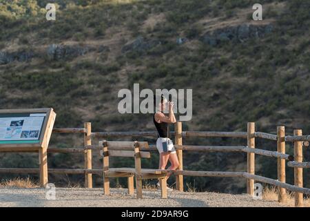 Giovane donna che guarda attraverso il binocolo ad un punto di osservazione con legno protezione nella foresta Foto Stock