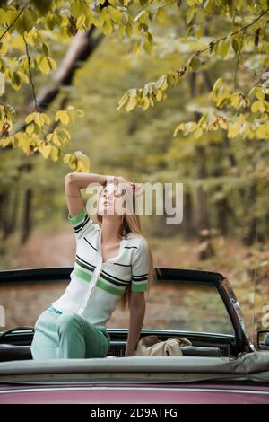 giovane donna elegante che tiene la mano sopra la testa mentre si posa dentro cabriolet con occhi chiusi Foto Stock