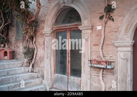 Una porta in legno e vetro di una casa in mattoni abbandonata con piante da arrampicata e decorazioni architettoniche (Corinaldo, Marche, Italia) Foto Stock
