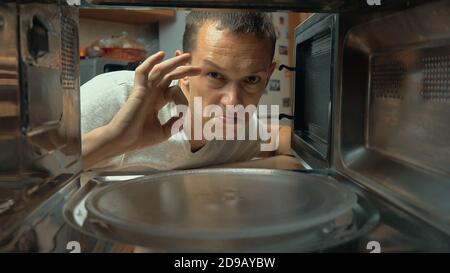 L'uomo apre il forno a microonde, guarda all'interno e mostra il segno OK. Indica la qualità del lavoro o della cottura. Riprese dall'interno. Foto Stock