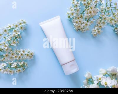 Vista dall'alto della confezione del tubo in plastica bianco per bottiglie. Sfondo blu e piccoli fiori bianchi. Tubo bianco in plastica lucida per medicina o cosmetici Foto Stock