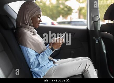 Sorridente Mussulmano nero imprenditore Browsing smartphone mentre Riding Car Su sedile posteriore Foto Stock