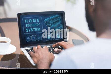 Uomo che usa il suo laptop con l'applicazione di sicurezza domestica Foto Stock