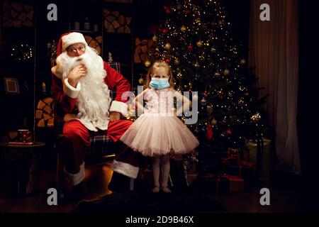 Babbo Natale e piccola ragazza arrabbiata la fanno indossare una maschera medica nelle vacanze di Natale e pandemia. Foto Stock