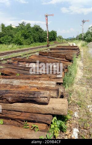 Dobra. Polonia. Il mucchio di vecchie traversine vaganti usate accatastate vicino alla pista ferroviaria. Antichi semafori vintage sullo sfondo. Foto Stock