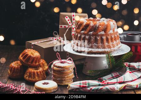 Assortimento di dolci di Natale fatti in casa e scatole regalo su un Tavolo rustico in legno con luci di Natale Foto Stock