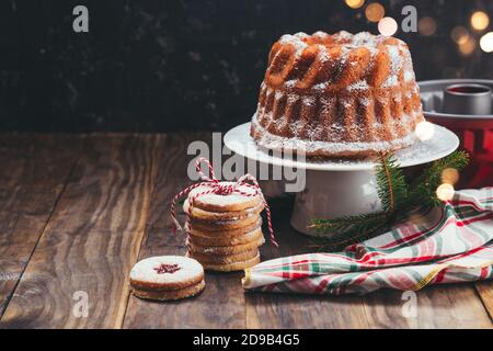 Torta di Natale fatta in casa e biscotti Linzer su un legno Tavolo con luci di Natale sullo sfondo Foto Stock