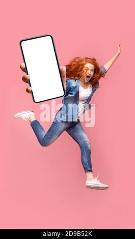 Positivo redhead girl saltando su rosa di sfondo per studio Foto Stock