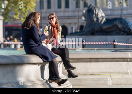 Westminster, Londra, Regno Unito. 4 Nov 2020. Londra ha goduto di una giornata luminosa ma fresca, con la gente che ha la possibilità di visitare prima del blocco COVID-19. Le femmine in Trafalgar Square godendo il tempo, seduti accanto alla fontana Foto Stock