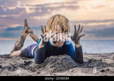 11.11 concetto di Black Friday. Ragazzo sorridente con il viso nero sporco seduto e giocando sulla spiaggia di sabbia nera. Vacanza estiva con i bambini. Black Friday, vendite Foto Stock