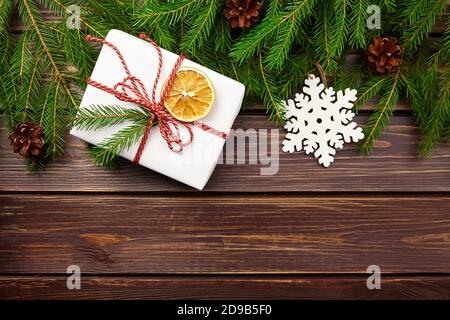Confezione regalo di Natale con rami di abete, coni e fiocchi di neve su fondo di legno Foto Stock