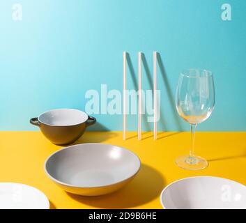 Vari piatti, cannucce e un bicchiere su sfondo giallo e blu Foto Stock