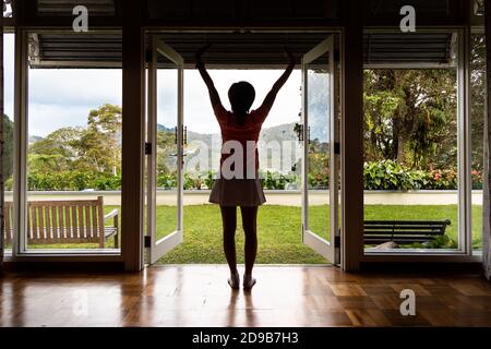 Le donne godono di un'alba rinfrescante con una scena verde dall'interno di casa Foto Stock