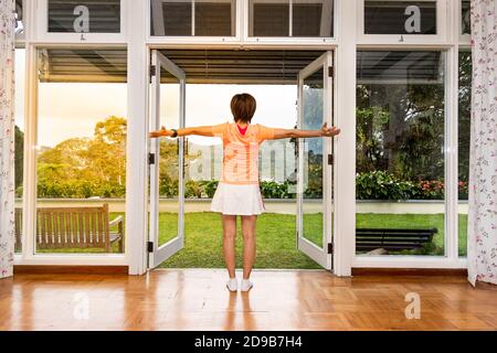 Le donne godono di un'alba rinfrescante con una scena verde dall'interno di casa Foto Stock