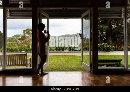 Donna che ammira il paesaggio naturale dalla porta con una tazza di caffè Foto Stock