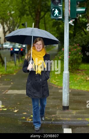 Donna con ombrello passa attraverso una luce verde pedone Foto Stock