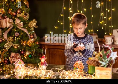 Un ragazzo si siede a un tavolo in una cucina di Natale decorata. Contiene un criceto o un mouse per animali domestici. Accoglienti serate invernali a casa. Concetto di Natale e nuovo anno Foto Stock