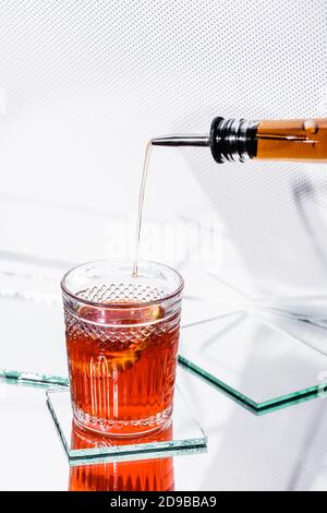 versare il whiskey in vetro con il cocktail del flacone con il dispenser su bianco Foto Stock