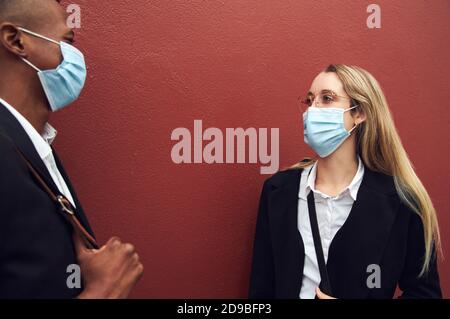 Uomo d'affari e Businesswoman che indossa maschere in piedi da parete fuori ufficio Durante la Pandemia di salute Foto Stock