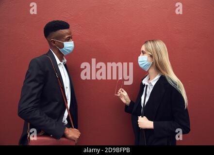 Uomo d'affari e Businesswoman che indossa maschere in piedi da parete fuori ufficio Durante la Pandemia di salute Foto Stock