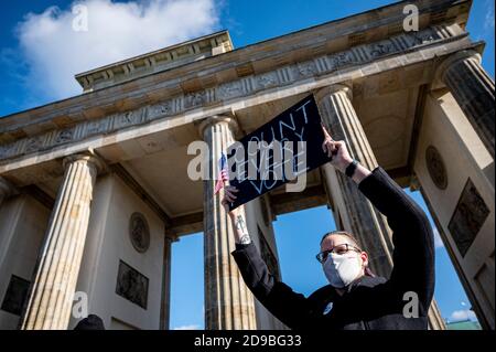 Berlino, Germania. 04Nov 2020. Un partecipante al rally, che si è tenuto sotto il motto "transizione pacifica della Presidenza e degli Stati Uniti democratici", ha tenuto un cartello davanti alla porta di Brandeburgo con la scritta "Conte ogni voto" e una mini bandiera statunitense. Più di 200 milioni di americani sono stati chiamati ad eleggere un nuovo presidente e i membri della Camera dei rappresentanti. Credit: Fabian Sommer/dpa/Alamy Live News Foto Stock