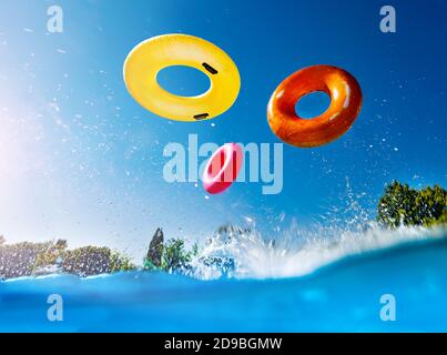 Foto d'azione nella piscina all'aperto con spruzzi e. onde di ciambelle gonfiabili buoys anelli che cadono giù sopra il cielo Foto Stock