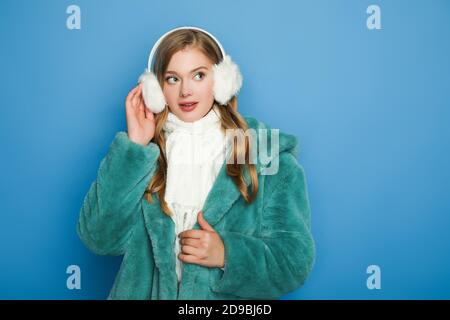 donna elegante con camice in pelliccia sintetica verde e cuffie auricolari isolato su blu Foto Stock