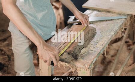 primo piano la mano del falegname che misura il legno usando il righello del nastro dei falegnami in officina Foto Stock