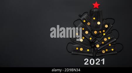 Albero di Natale fatto da maschere viso e oro confetti decorazione festa. Maschere facciali su sfondo nero. 2021 biglietto d'invito per Capodanno con copia Foto Stock