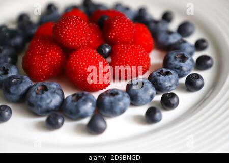 Fragole rosse, more e mirtilli su un piatto bianco. Composizione, primo piano, texture. Foto Stock