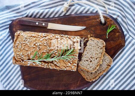 Il pane senza glutine di grano saraceno con una crosta dorata, cosparso di semi di girasole, giace su un tavolo di legno. Ricetta sana fatta in casa. Grani di verde Foto Stock