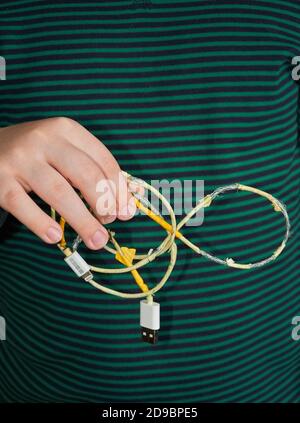 Il bambino tiene in mano un vecchio cavo USB strappato. Primo piano Foto Stock