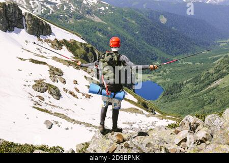 Uomo avventuriero in montagna escursioni in montagna viaggiando da solo con grande zaino ha scalato la cima di alte rocce innevate e valli con un lago Foto Stock