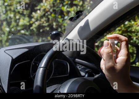 Mani umane con spray imbevuto di alcool per disinfettare il volante della vettura. Irrorazione prevenire l'infezione del coronavirus Covid-19. Foto Stock