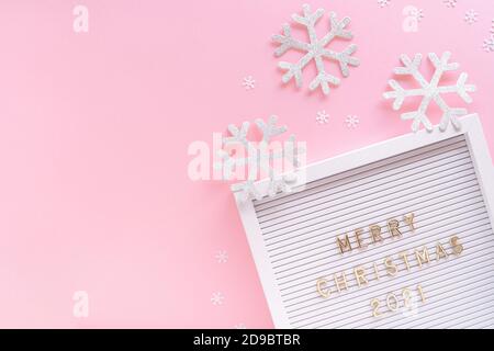 Lavagna con auguri di buon Natale 2021, fiocco di neve decorativo su sfondo rosa pastello girly. Composizione cornice Natale. Disposizione piatta, spazio di copia Foto Stock