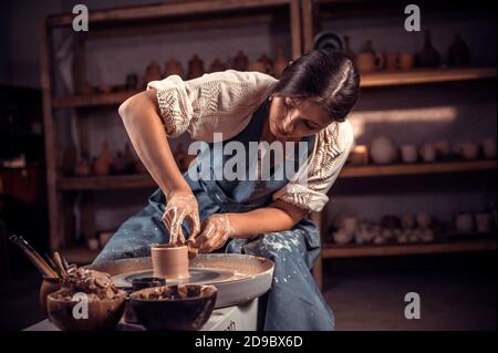 Vasaio professionale ed elegante che lavora sulla ruota del vasaio con creta cruda con le mani. Artigianato nazionale. Foto Stock