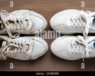 Un paio di vecchie sneaker bianche sporche davanti a una nuova sneaker pulita su sfondo marrone. Concetti passati e futuri, vecchi e nuovi. Vista dall'alto. Foto Stock