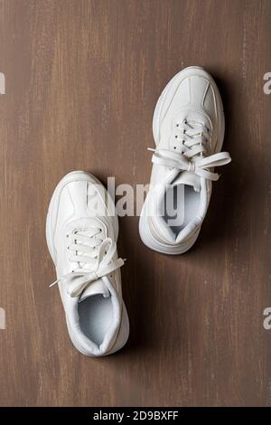 Paio di sneaker bianche con lacci allacciati su sfondo marrone. Nuove scarpe unisex chunky per uno stile di vita attivo, fitness e sport. Spazio di copia. Vista dall'alto. Foto Stock