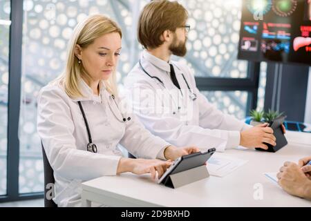 Incontro dei medici e briefing. Team medico concentrato, donna e uomo caucasico, utilizzando tablet computer, seduti insieme al tavolo su medico Foto Stock